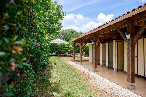 Instalaciones de baño al aire libre junto a la tienda safari Villatent Wood en Camping Lestaubière, Francia, con vegetación.