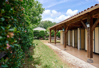 Servizi igienici esterni vicino alla tenda safari Villatent Wood al Camping Lestaubière, Francia, circondati dal verde.