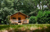 La tienda safari Villatent Nomad en Camping Lestaubière, Francia, rodeada de árboles y vegetación verde.