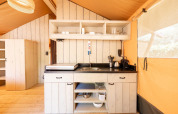 Lichte, moderne kitchenette in een safari tent Villatent Nomad met houten planken, kasten en keukenbenodigdheden.