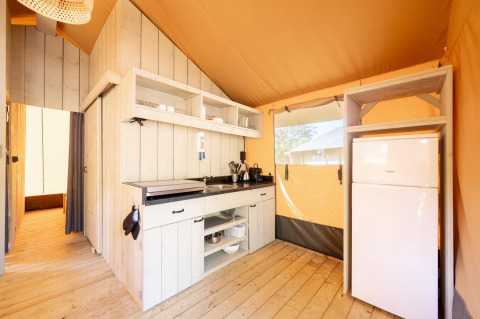 Interior de una tienda safari Villatent Nomad con cocina equipada y nevera sobre suelo de madera.