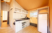 Interior de una tienda safari Villatent Nomad con cocina equipada y nevera sobre suelo de madera.