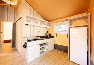 Interior de una tienda safari Villatent Nomad con cocina equipada y nevera sobre suelo de madera.