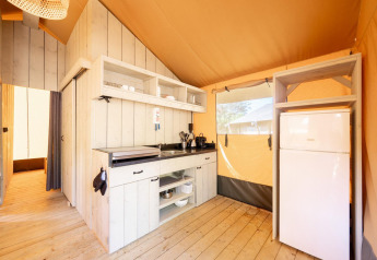 Interior of a Villatent Nomad safari tent featuring a fully equipped kitchen and fridge on wooden floor.