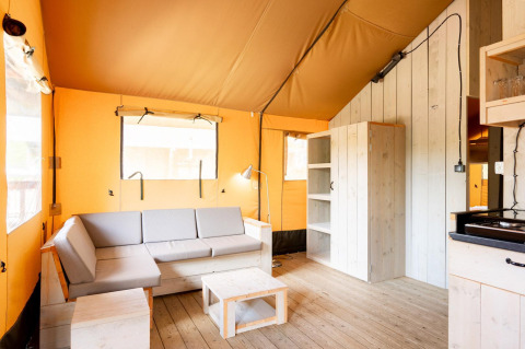 Interior de una tienda safari Villatent Nomad con suelo de madera, sofá claro, estanterías y luz natural.