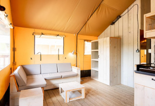 Interior de una tienda safari Villatent Nomad con suelo de madera, sofá claro, estanterías y luz natural.