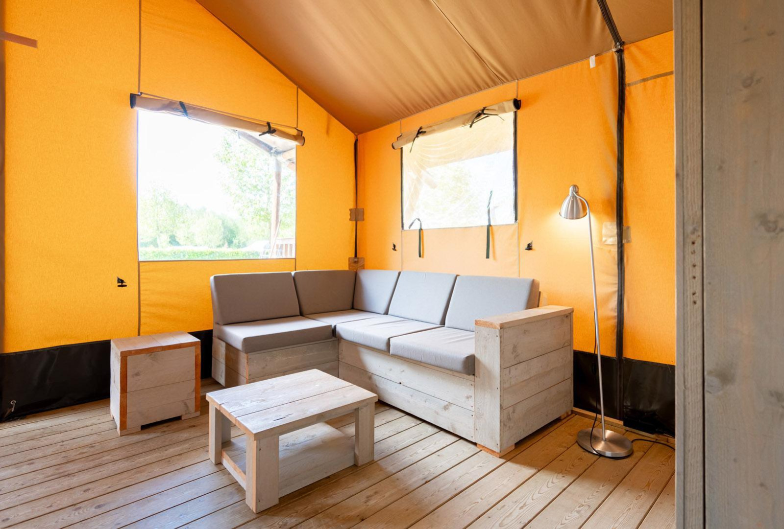 Interieur van safaritent Villatent Nomad met hoekbank, houten vloer en gele tentwanden.
