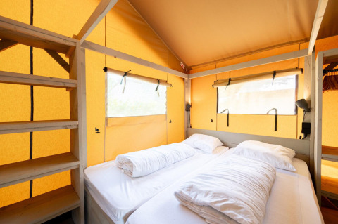 Vista interna della tenda safari Villatent Nomad con due letti singoli, scaffali e pareti gialle.