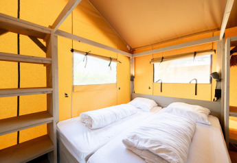 Innenansicht eines Safari-Zelts Villatent Nomad mit zwei Betten, Regalen und großen Fenstern.