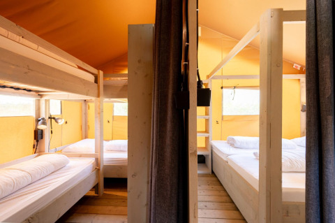 Interior de la tienda safari Villatent Nomad con literas, camas dobles, suelo de madera y paredes amarillas.