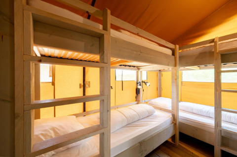 Vista interior de una tienda safari Villatent Nomad con literas de madera y ambiente cálido amarillo.