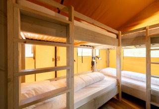 Binnenaanzicht van een Villatent Nomad safaritent met houten stapelbedden en warme gele stof.