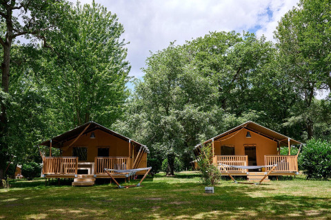 Dos tiendas safari con porches en Camping Lestaubière, Francia, rodeadas de verdes árboles frondosos.