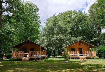 Twee safaritenten met veranda bij Camping Lestaubière in Frankrijk, omgeven door groene natuur.