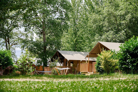 Safaritenten van Villatent Nomad op Camping Lestaubière in Frankrijk, omringd door groene bomen.