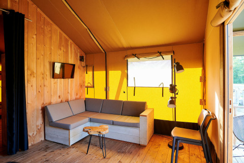 Vue intérieure d'une tente safari avec murs en bois, canapé confortable et lumière naturelle aux Pays-Bas.