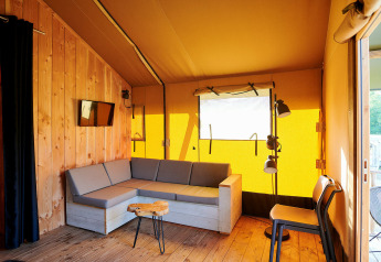 Interieur van een safaritent met houten wanden, comfortabele bank en veel daglicht in Nederland.