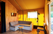 Interior view of a safari tent with wooden walls, a cozy sofa, and natural light in the Netherlands.