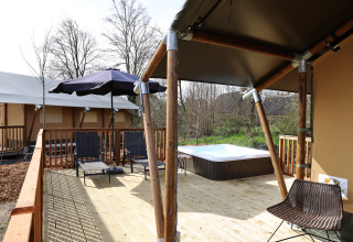 Terrasse extérieure avec jacuzzi, transats et parasol à Safari Tent Wellness, Holiday Park Sallandshoeve, Pays-Bas.