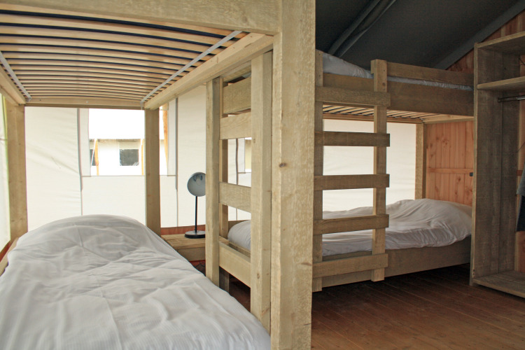 Vista interior de una tienda safari con litera y cama individual en Holiday Park Sallandshoeve, Países Bajos.