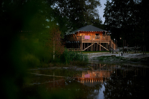 Tente safari éclairée au bord d'un étang au crépuscule au Holiday Park Sallandshoeve, Pays-Bas.