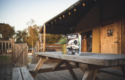 Terrasse der Safaricottage XL mit Holztisch, Bank und Magazin im Holiday Park Sallandshoeve, Niederlande.