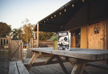 Terrasse extérieure du Safaricottage XL avec table, bancs et magazine au Holiday Park Sallandshoeve, Pays-Bas.