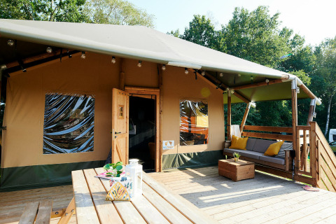 Grande tente safari avec terrasse en bois et coin salon, Holiday Park Sallandshoeve, Pays-Bas, entourée d’arbres.