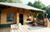 Grande tente safari avec terrasse en bois et coin salon, Holiday Park Sallandshoeve, Pays-Bas, entourée d’arbres.