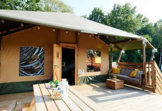 Grande tente safari avec terrasse en bois et coin salon, Holiday Park Sallandshoeve, Pays-Bas, entourée d’arbres.