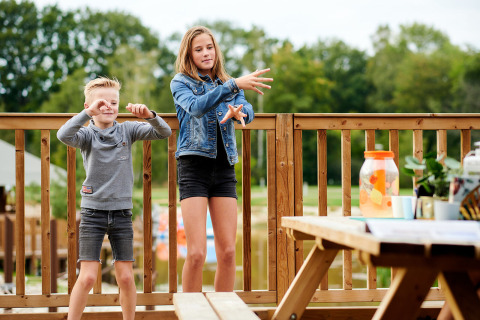 Twee kinderen spelen op een houten terras bij Safaricottage XL, Holiday Park Sallandshoeve, Nederland.