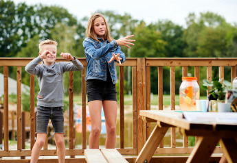 To børn leger på en træterrasse ved Safaricottage XL i Holiday Park Sallandshoeve, Holland, sommerdag.
