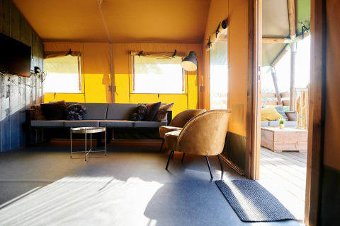 Moderne opholdsstue i Safaricottage XL telt i Holiday Park Sallandshoeve, med sofa, stol og lysindfald.