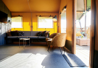 Lichte woonkamer van Safaricottage XL tent bij Holiday Park Sallandshoeve, met bank en fauteuil.