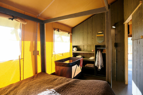 Interior de una Safaricottage XL con cama, cuna y armario en Holiday Park Sallandshoeve, Países Bajos.