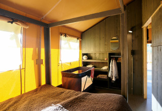 Interno di una Safaricottage XL con letto, culla e armadio all'Holiday Park Sallandshoeve, Paesi Bassi.