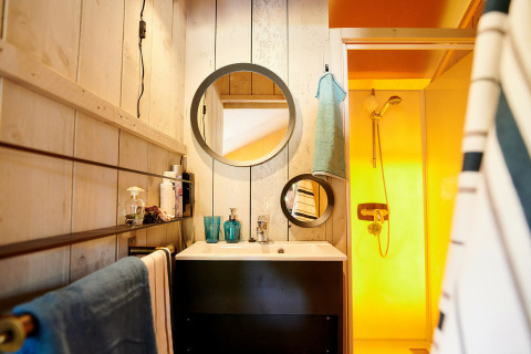 Baño en una Safaricottage XL en Holiday Park Sallandshoeve con espejos redondos, toallas y ducha amarilla.