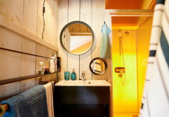 Badkamer in een Safaricottage XL op Vakantiepark Sallandshoeve met ronde spiegels, handdoeken en gele douche.