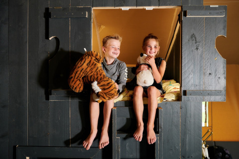 Dos niños se sientan con peluches en una litera del Safaricottage XL, Holiday Park Sallandshoeve, Países Bajos.