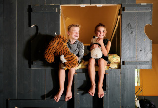 Zwei Kinder sitzen mit Kuscheltieren im Safaricottage XL im Ferienpark Sallandshoeve, Niederlande.