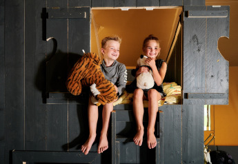 Two children sit with stuffed animals in a cabin bunk at Safaricottage XL, Holiday Park Sallandshoeve.