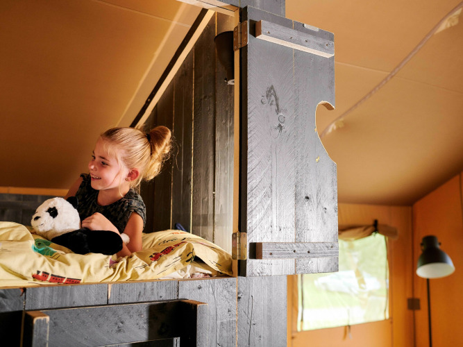 Fille avec une peluche panda sur un lit en hauteur dans une Safaricottage XL au Holiday Park Sallandshoeve, Pays-Bas.