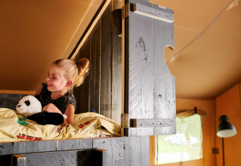 Girl with a panda plush toy on a loft bed in Safaricottage XL at Holiday Park Sallandshoeve, Netherlands.