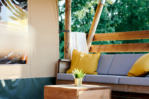 Zona de descanso al aire libre en una tienda Safaricottage XL con cojines amarillos en Holiday Park Sallandshoeve.