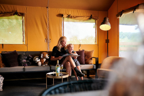 Madre e hija se relajan en una Safaricottage XL en Holiday Park Sallandshoeve, Países Bajos, rodeadas de cojines.