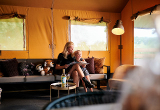 Mor og datter hygger i en safaricottage XL på Holiday Park Sallandshoeve i Holland, omgivet af puder og tøjdyr.