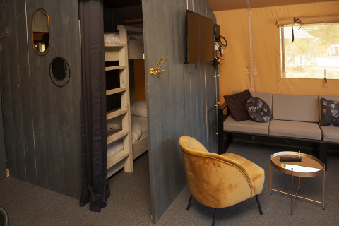 Interior de la Safaricottage XL con literas, sofá, sillón amarillo y TV en el Holiday Park Sallandshoeve.