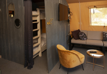 Interieur van Safaricottage XL met stapelbed, bank, gele stoel en tv bij Holiday Park Sallandshoeve.