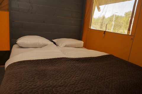 Letto matrimoniale accogliente con coperta marrone in una tenda Safaricottage XL a Holiday Park Sallandshoeve.