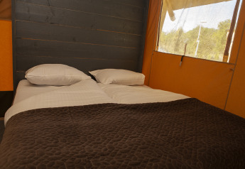 Cama doble cómoda con manta marrón en una tienda Safaricottage XL en Holiday Park Sallandshoeve, Países Bajos.